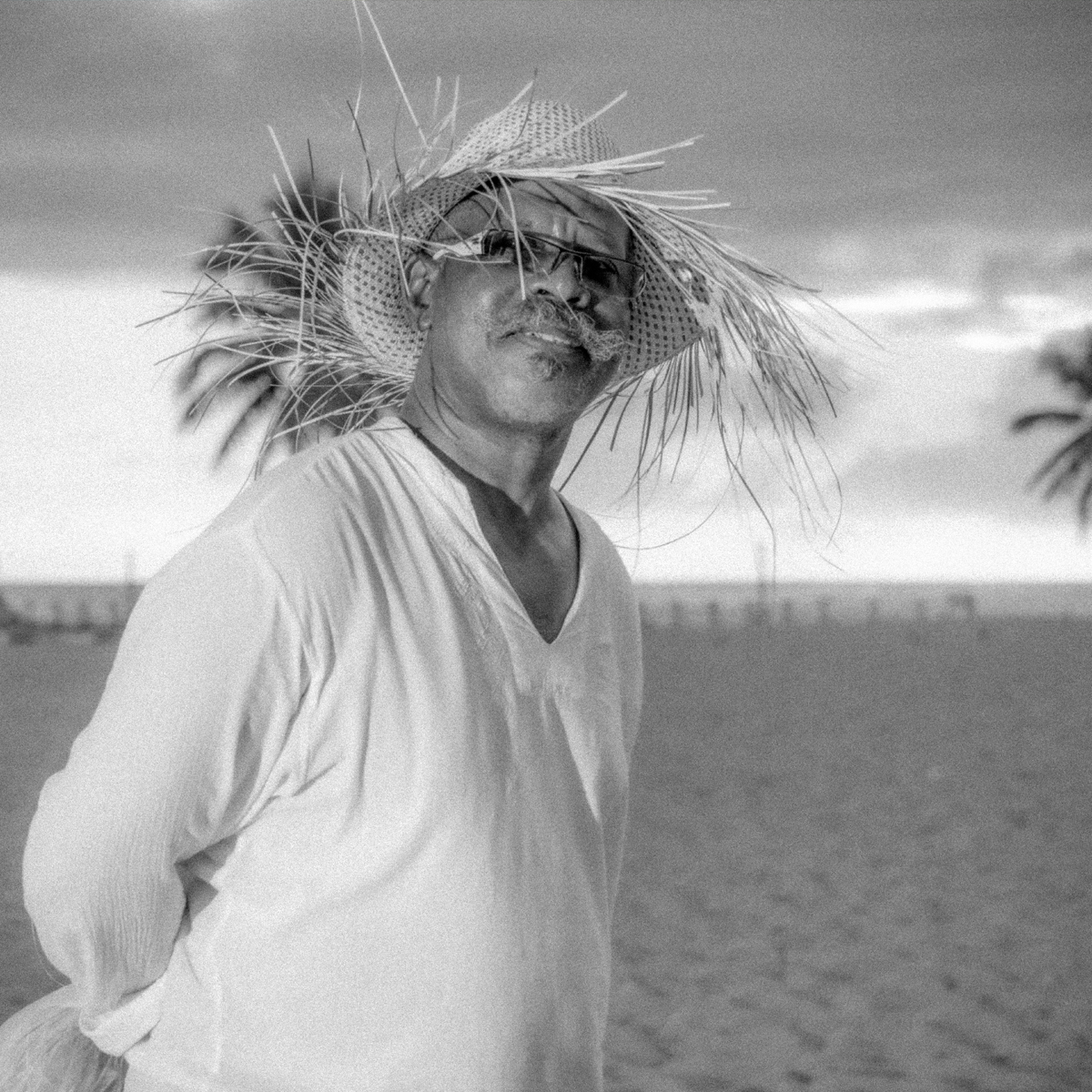 Ocean Portrait: Raffia and Diffused Light Luxury beach portrait in Santo Domingo: man with raffia accessory, gray ocean light, dark sunglasses, white texture and Caribbean wind