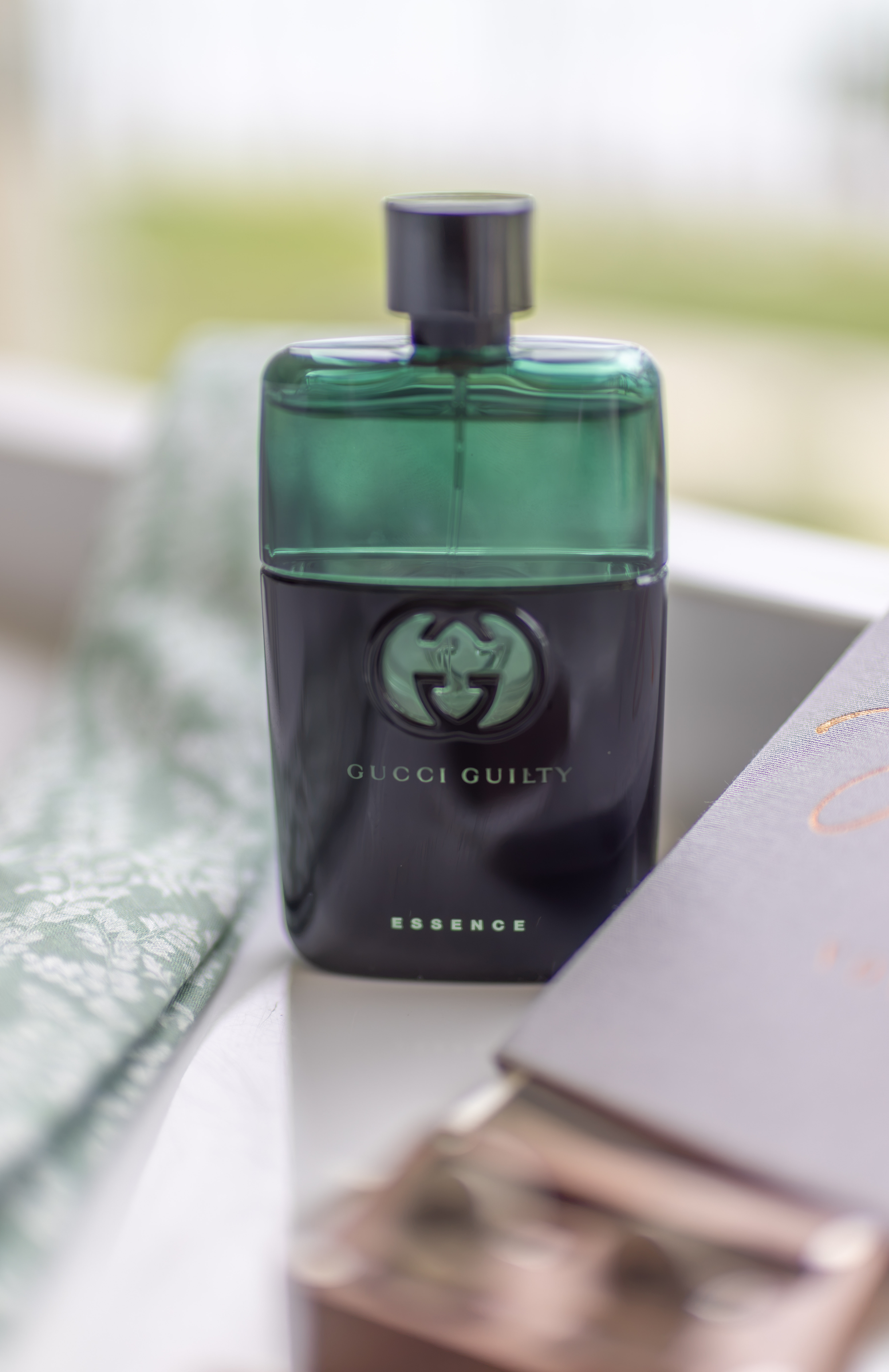 Luxury fragrance with refined editorial composition Green and black Gucci Guilty Essence fragrance bottle on white linen with notebook, luxury product photography in Santo Domingo