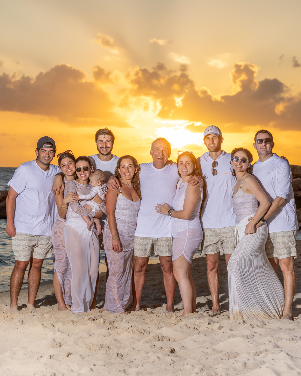 Familia de diez personas en sesión de playa al atardecer en Santo Domingo, vistiendo tonos de morado y crema, rodeados de luz dorada del Caribe