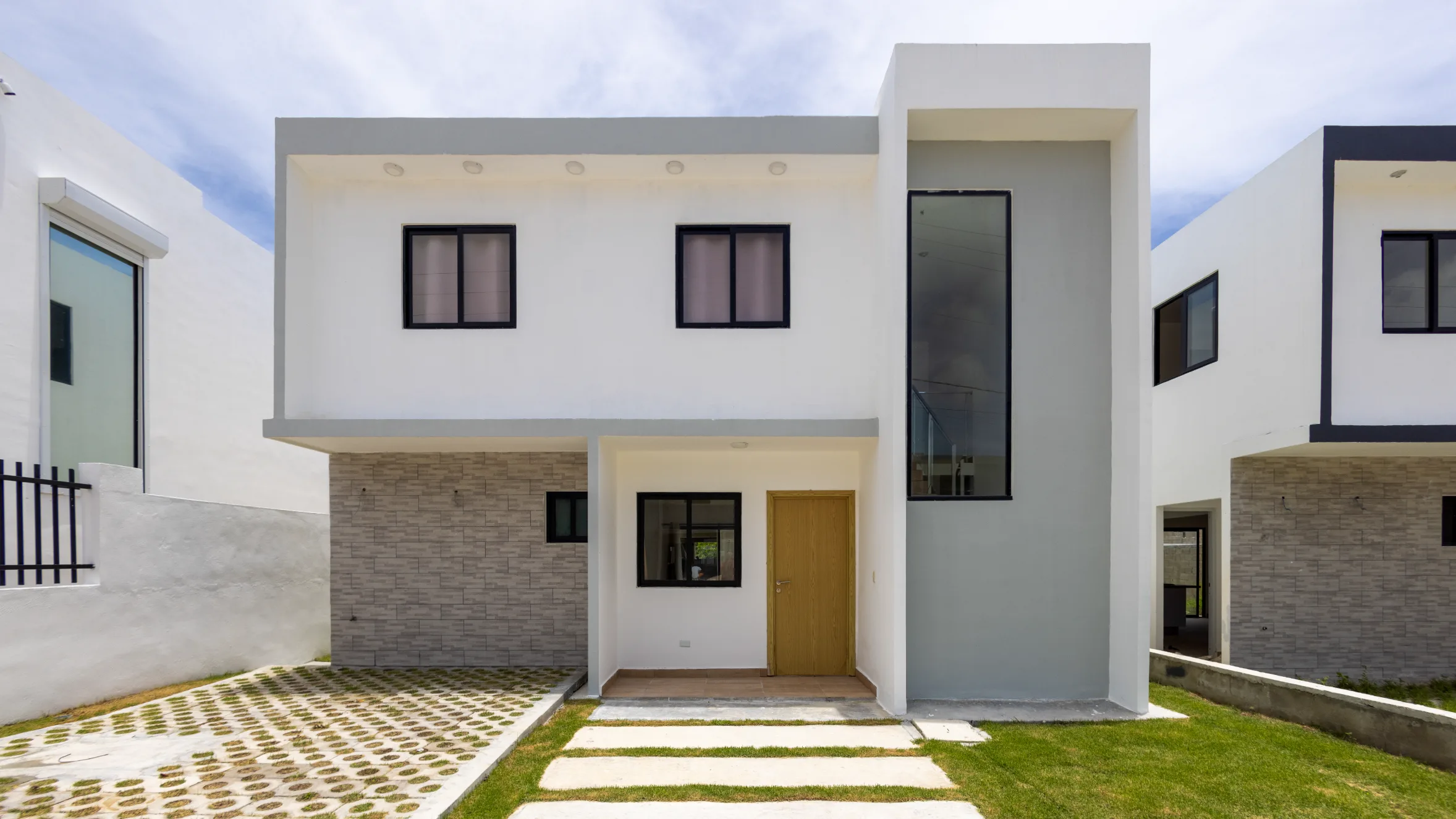 Modern residence in Santo Domingo with midday light Two-story modern residence with white facade, brick details, and pedestrian entry in Santo Domingo. Real estate photography with midday natural light.