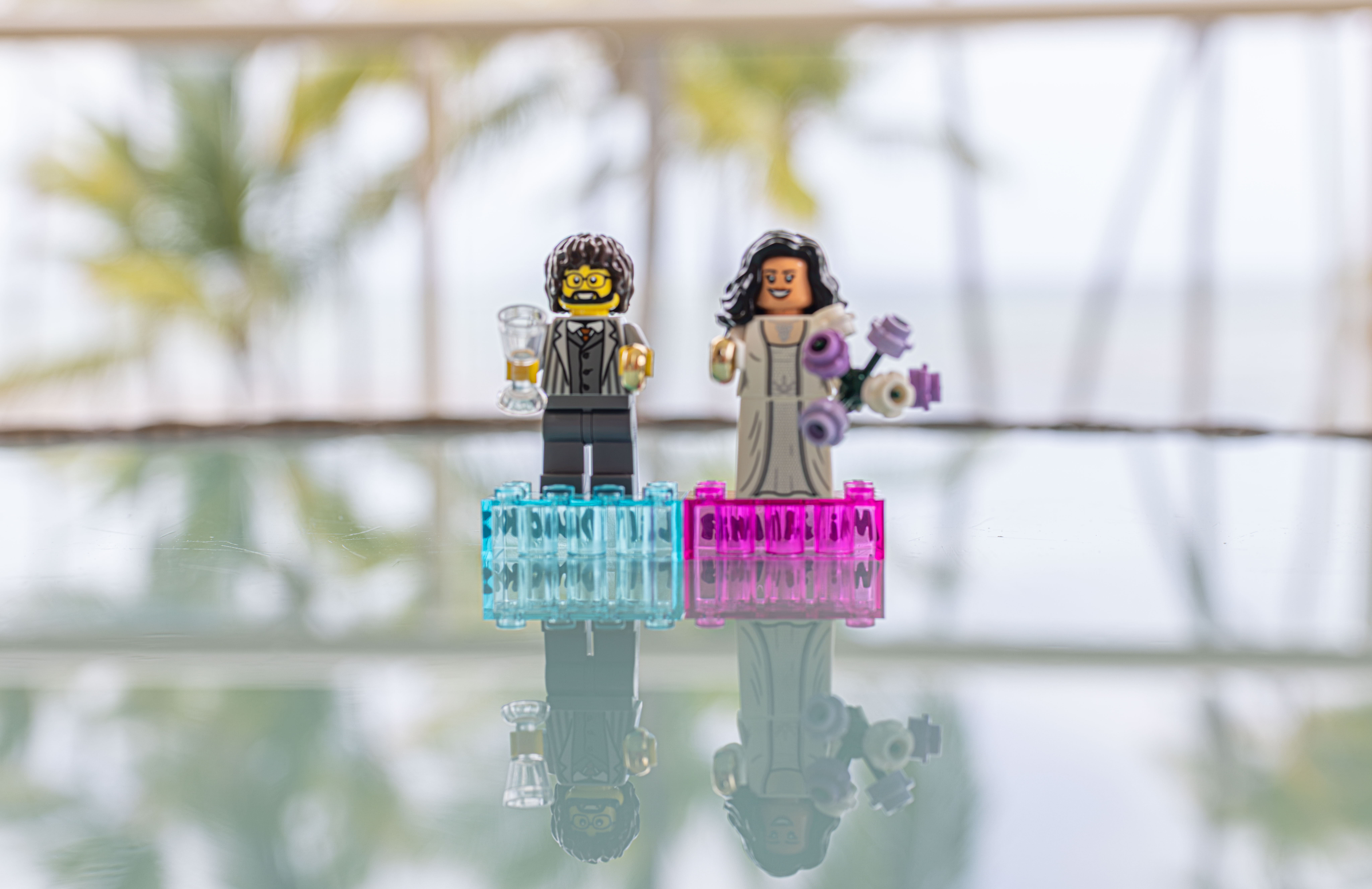 Miniature wedding proposal: playful love reflected LEGO bride and groom figures reflected in crystal water with purple flowers, representing creative proposal photography in Santo Domingo
