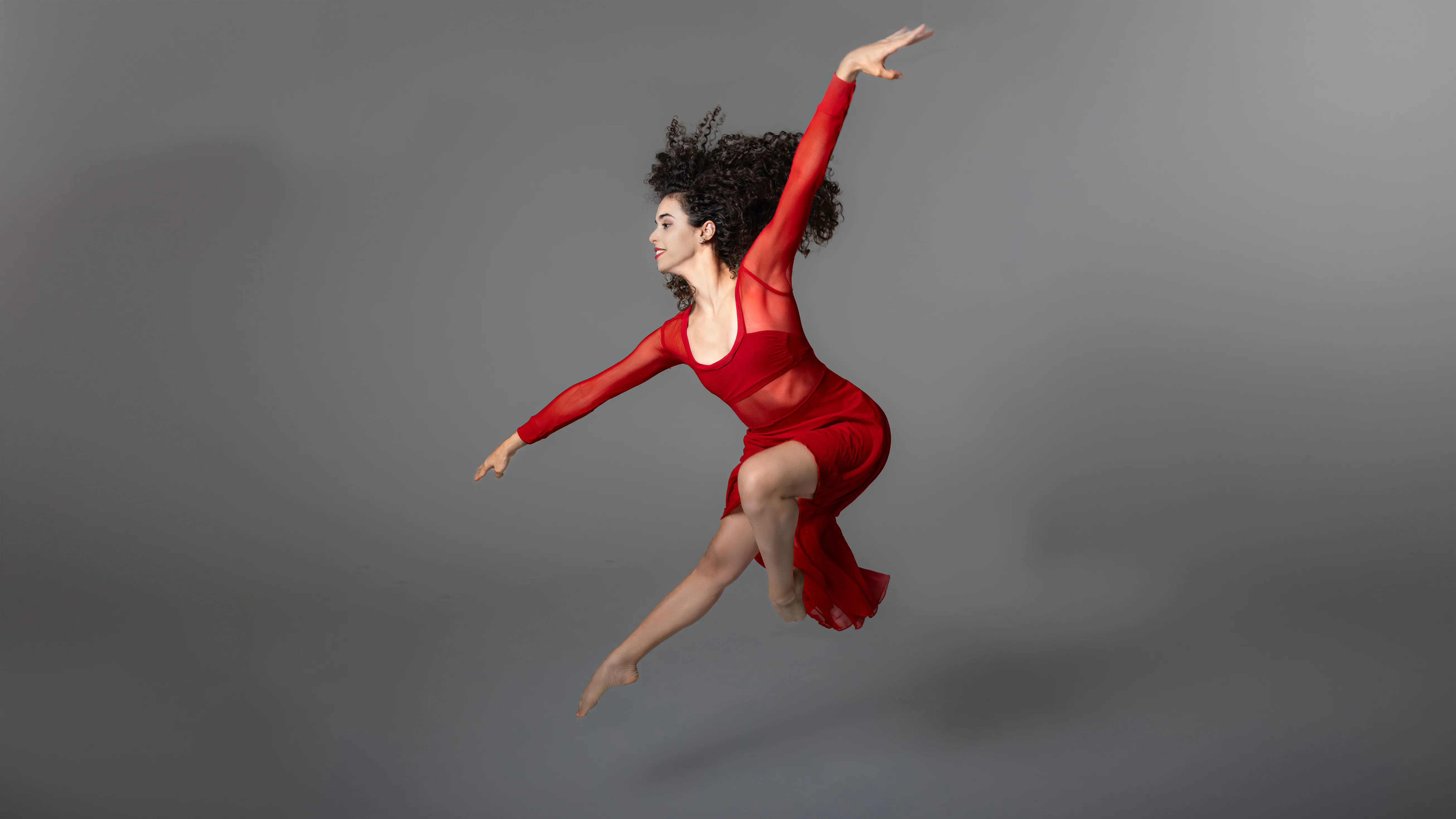 Bailarina en vuelo — Retrato artístico Bailarina en vuelo con traje rojo contra fondo gris neutro; fotografía artística de movimiento en estudio Santo Domingo
