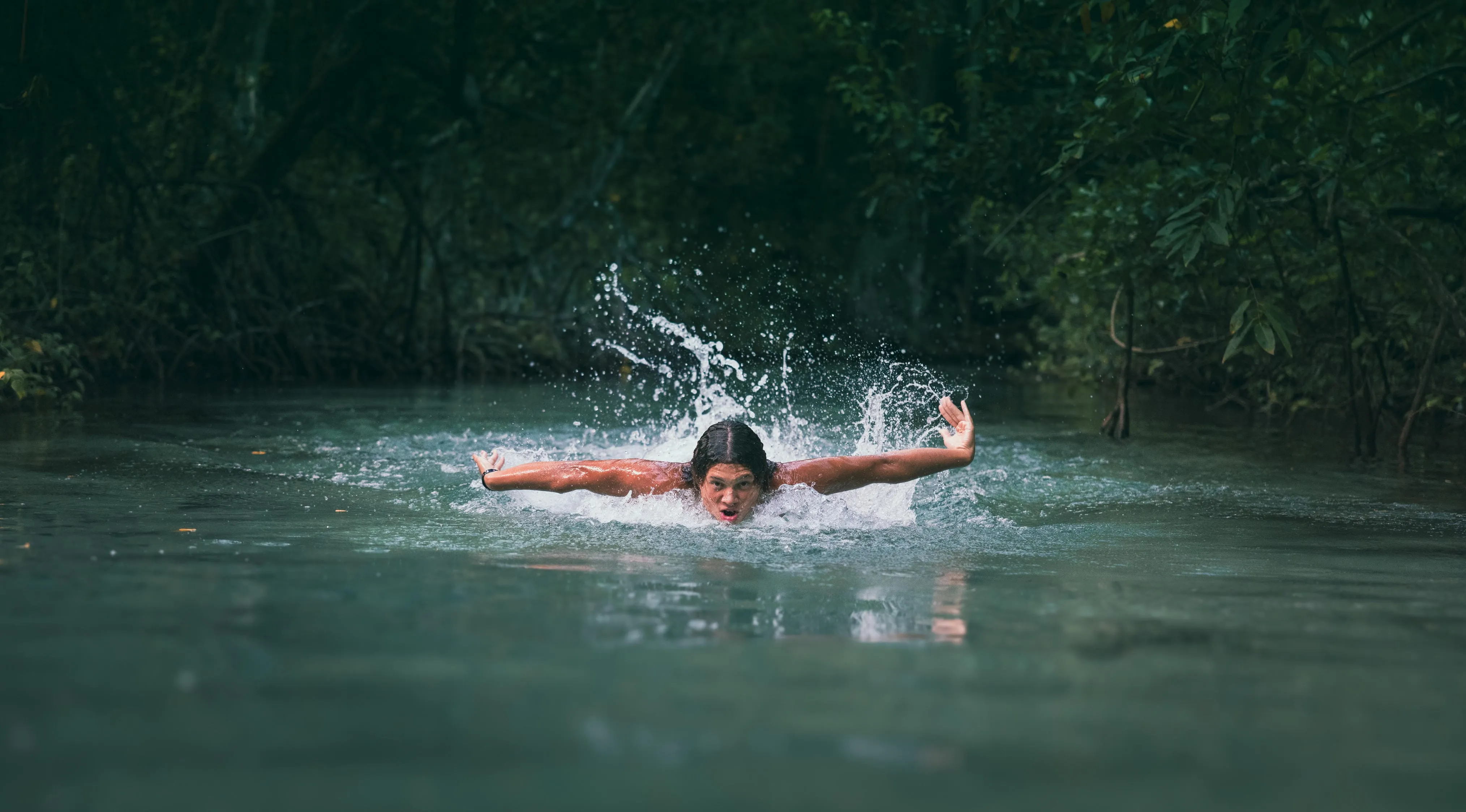 Freedom in the water: family river session Family river session: child swimming in crystalline waters with open arms among tropical vegetation in Santo Domingo
