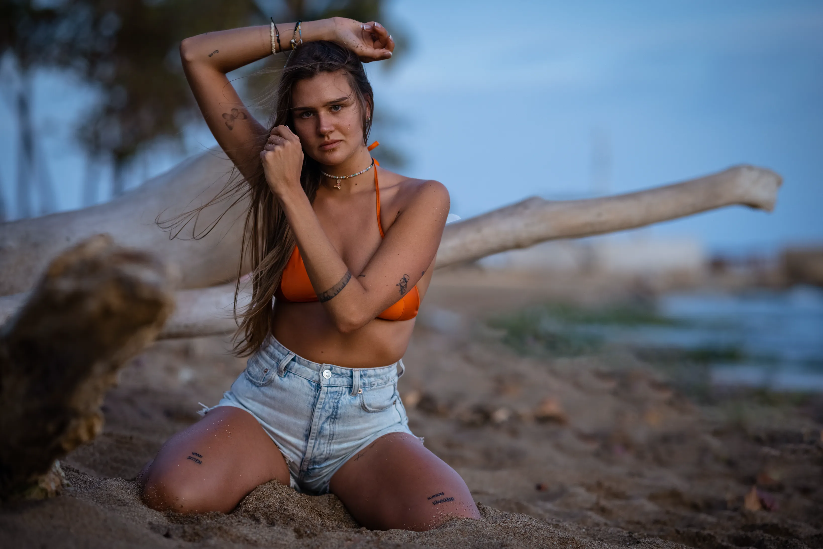Beach Portrait at Sunset Luxury portrait session on Santo Domingo beach: woman posing on sand beside weathered driftwood in golden sunset light