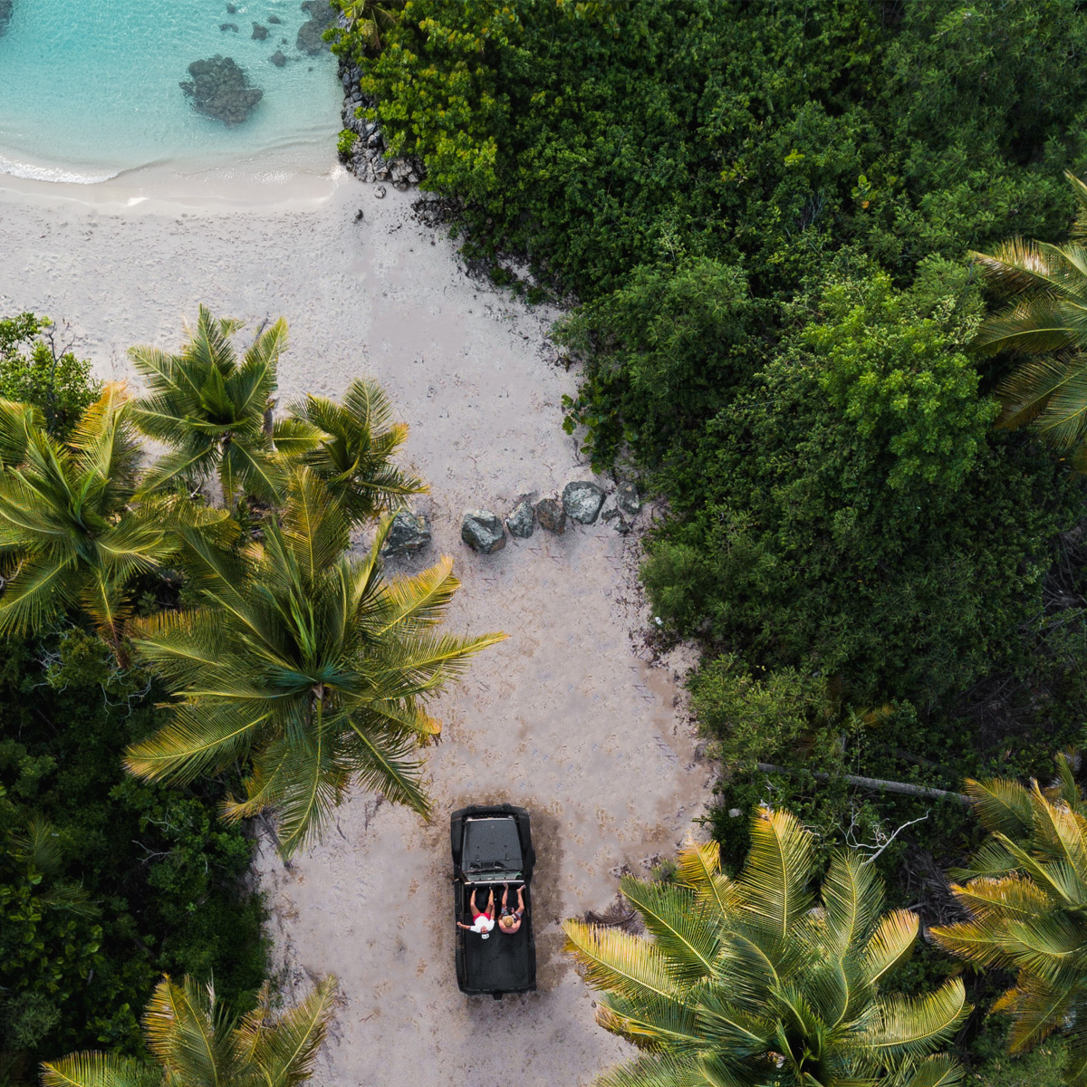 Sesión Familiar Desde el Aire en Playa Caribeña Auto negro estacionado en arena blanca de playa caribeña con familia sonriendo, rodeado de manglares y agua turquesa en sesión de fotografía familiar