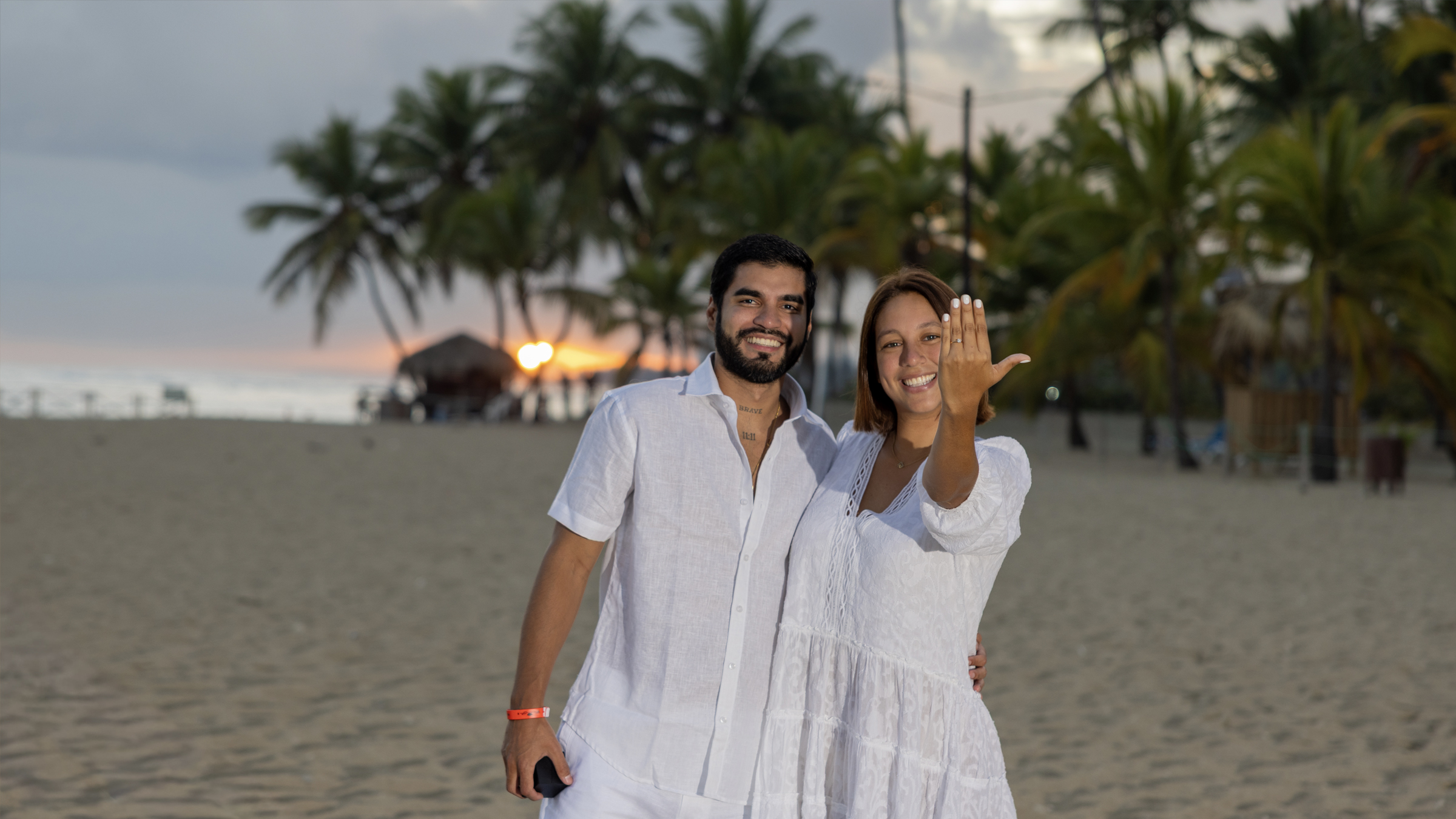 Marriage proposal under Caribbean sunset Couple in marriage proposal on Santo Domingo beach at sunset, woman showing ring with surprised smile, golden light framed by palm trees