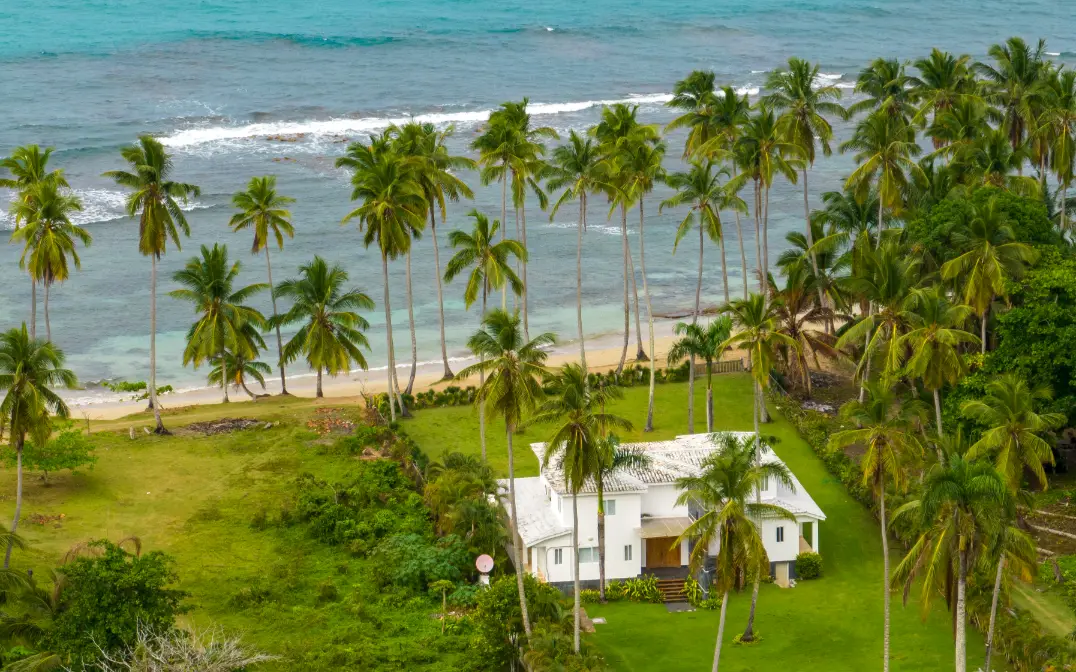 Coastal beach with palms and house White house surrounded by tall palms overlooking turquoise beach with waves, family beach session Dominican Republic